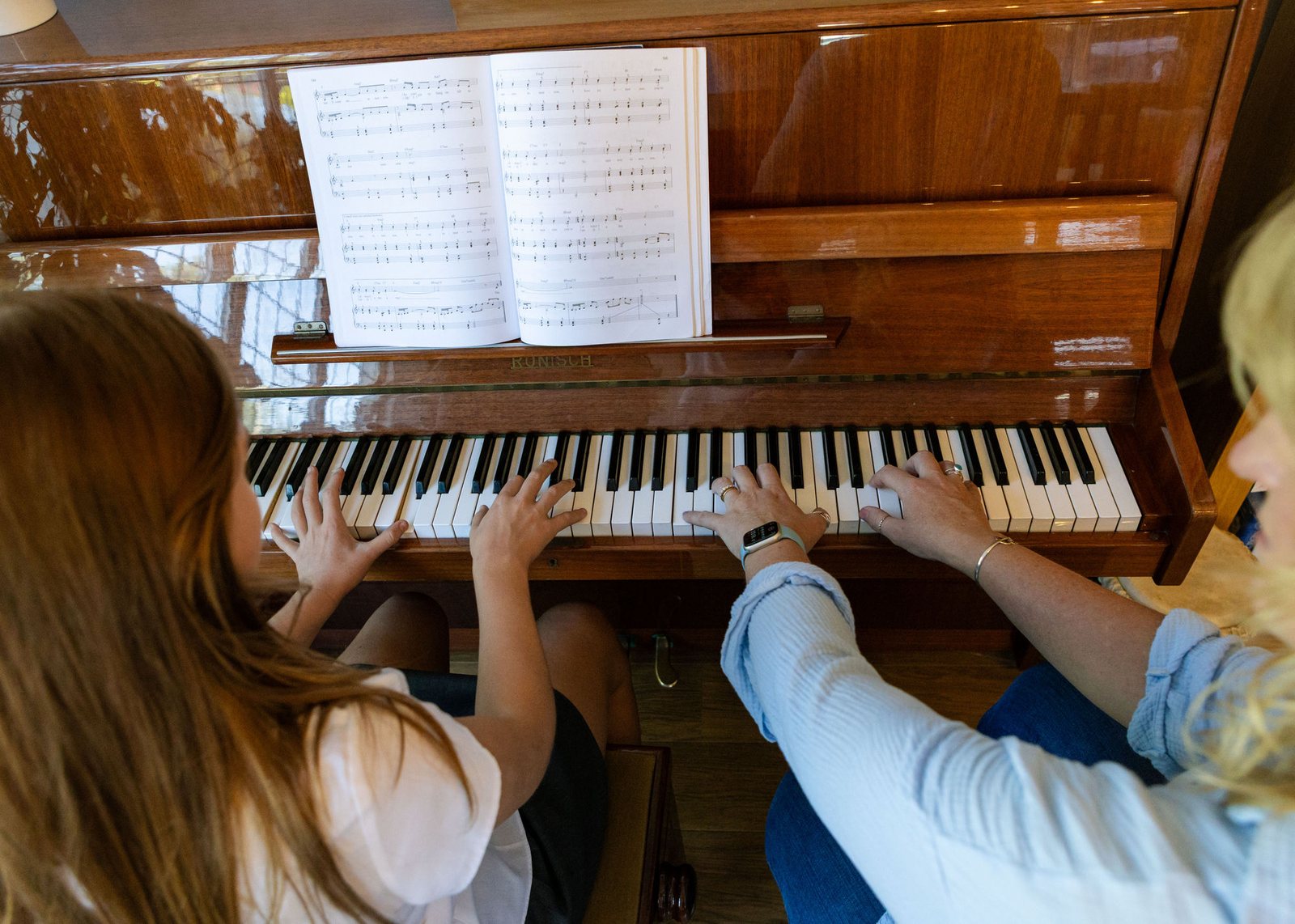 Two people sharing a piano stool, working through a piece together